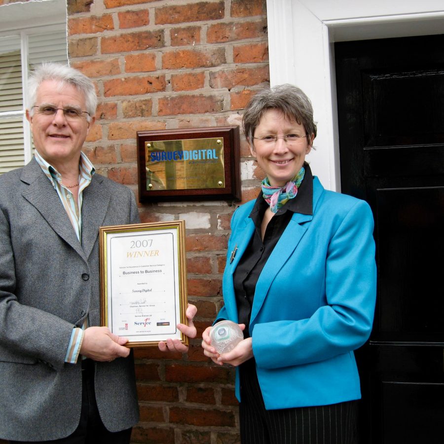 Two people holding a framed award certificate outside EMD office